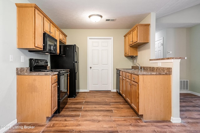 kitchen featuring visible vents, a sink, black appliances, and wood finished floors