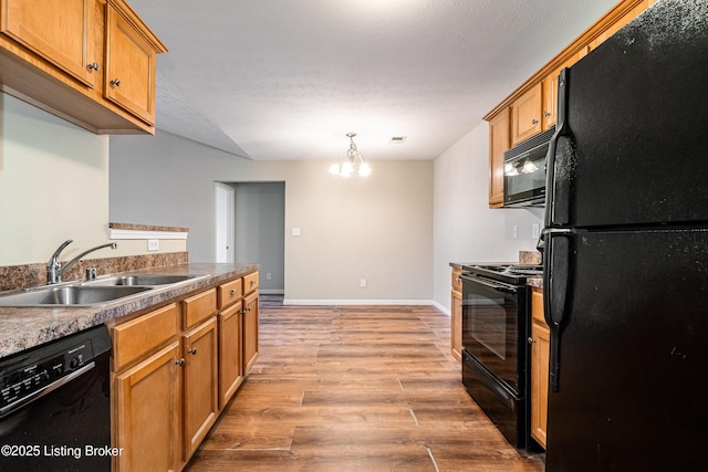 kitchen with baseboards, a sink, black appliances, light wood-style floors, and brown cabinets