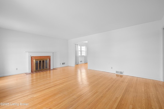 unfurnished living room featuring light wood finished floors, visible vents, and a brick fireplace