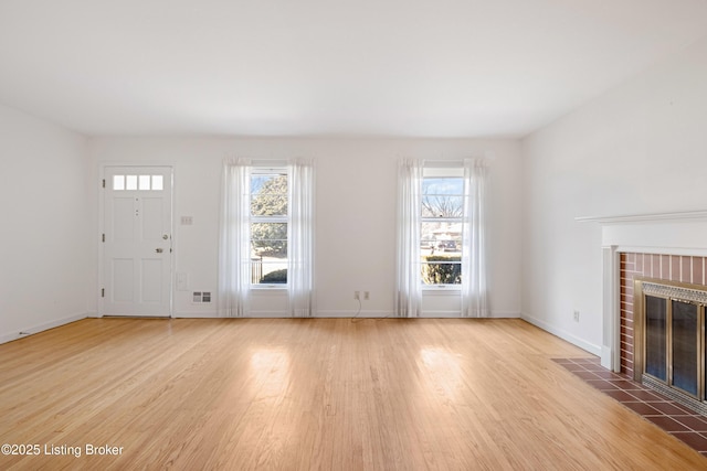 unfurnished living room featuring visible vents, light wood-style flooring, a brick fireplace, and baseboards