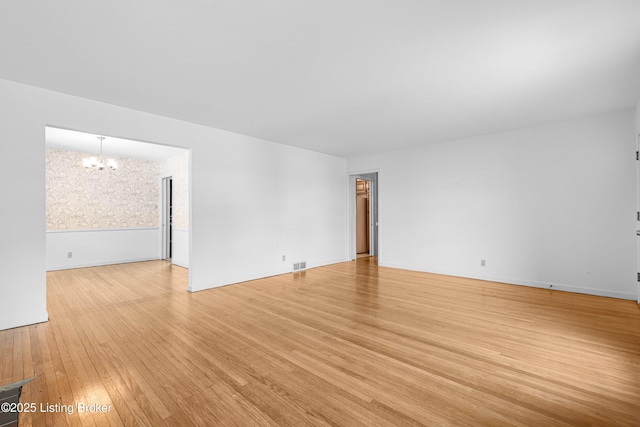 unfurnished room featuring visible vents, a notable chandelier, and light wood finished floors