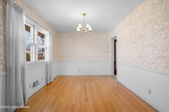 unfurnished room with wallpapered walls, an inviting chandelier, light wood-style floors, and a wainscoted wall