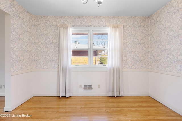 unfurnished room featuring wallpapered walls, visible vents, a wainscoted wall, and light wood-type flooring