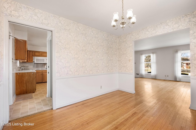 unfurnished dining area with a notable chandelier, wallpapered walls, light wood-style floors, and a wainscoted wall