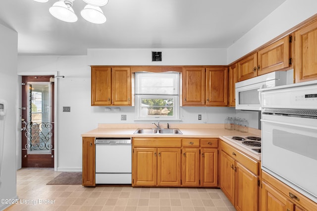 kitchen with a sink, white appliances, brown cabinets, and light countertops