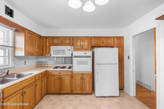 kitchen featuring visible vents, light countertops, brown cabinets, white appliances, and a sink