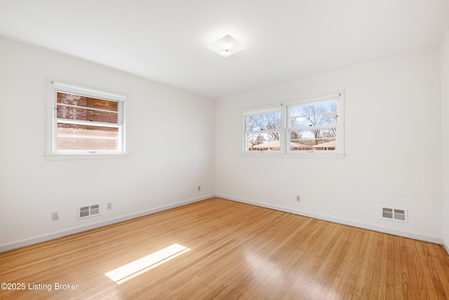 empty room with wood finished floors, a healthy amount of sunlight, and visible vents