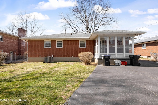 rear view of property featuring cooling unit, brick siding, a yard, and a sunroom