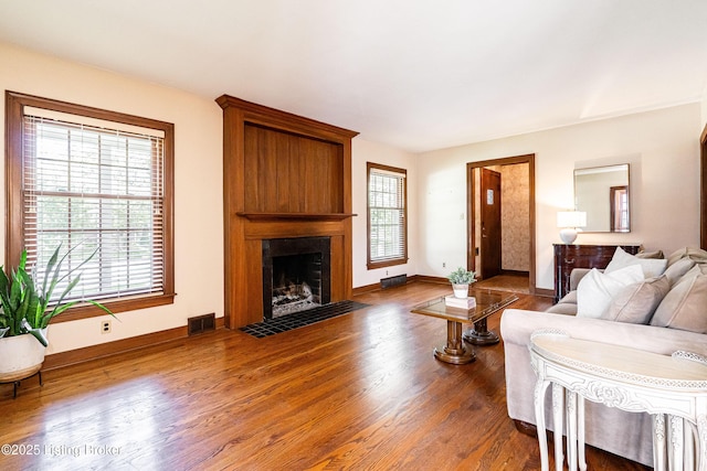 living room with a fireplace, wood finished floors, visible vents, and baseboards