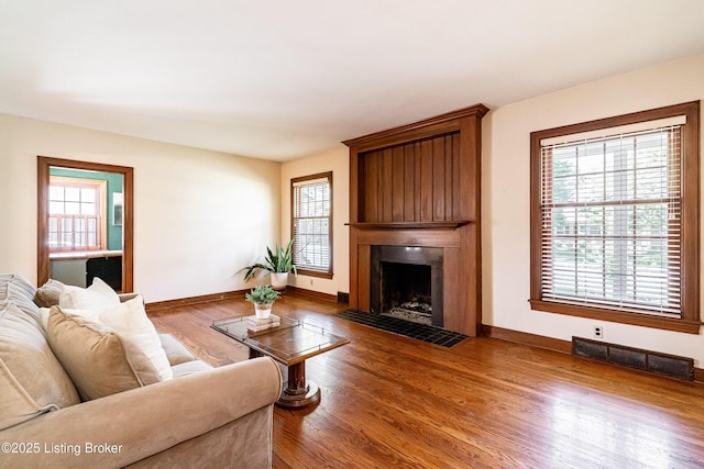 living room featuring baseboards, wood finished floors, visible vents, and a large fireplace