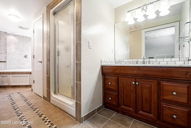 bathroom featuring tile patterned floors, a stall shower, baseboards, a bathtub, and vanity