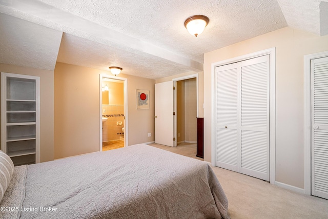 bedroom with baseboards, multiple closets, light carpet, ensuite bathroom, and a textured ceiling