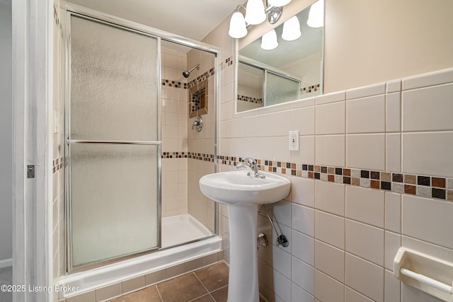 bathroom featuring a sink, tile patterned flooring, a shower stall, tile walls, and tasteful backsplash