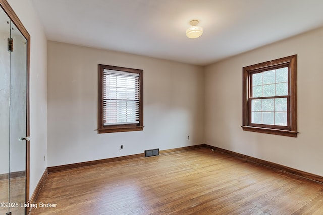 empty room with wood finished floors, visible vents, and baseboards