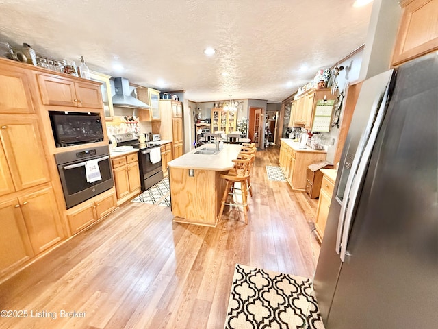 kitchen featuring light brown cabinets, light wood-style flooring, appliances with stainless steel finishes, and wall chimney exhaust hood