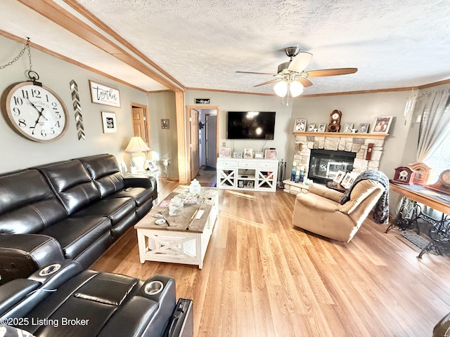 living room featuring a textured ceiling, a stone fireplace, wood finished floors, and ornamental molding