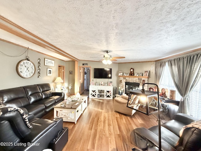 living room featuring wood finished floors, a ceiling fan, a fireplace, ornamental molding, and a textured ceiling