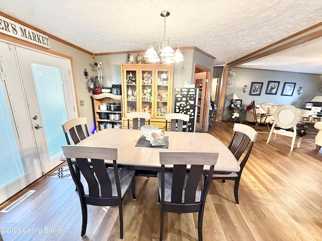 dining area featuring a notable chandelier, visible vents, light wood-style flooring, and a textured ceiling