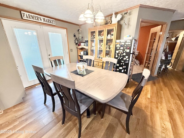 dining room featuring light wood finished floors, a notable chandelier, french doors, and ornamental molding