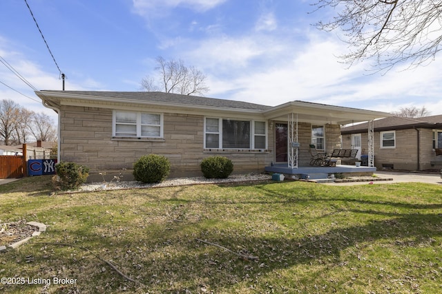 view of front of house featuring fence, roof with shingles, covered porch, a front lawn, and stone siding