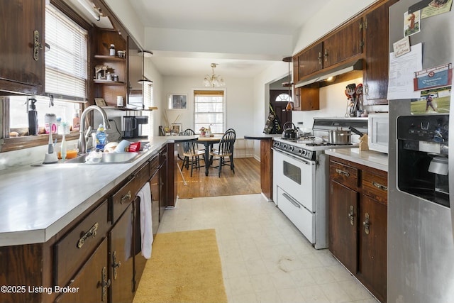 kitchen with under cabinet range hood, dark brown cabinetry, light floors, white appliances, and a sink