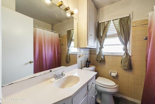 full bath featuring vanity, tile walls, toilet, and a healthy amount of sunlight