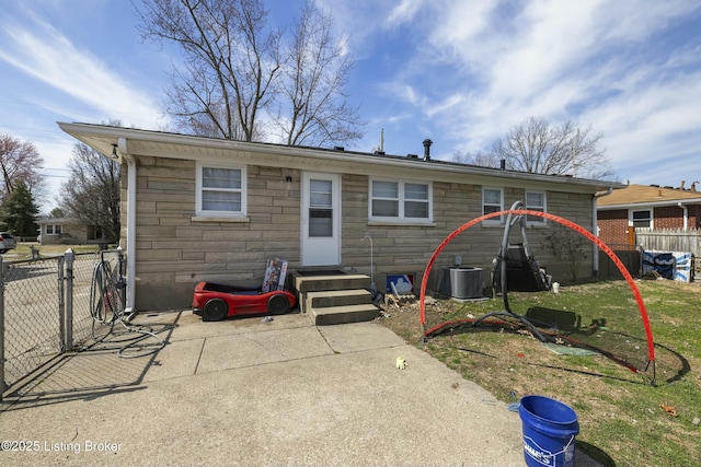 rear view of property with fence, entry steps, central AC, a yard, and stone siding