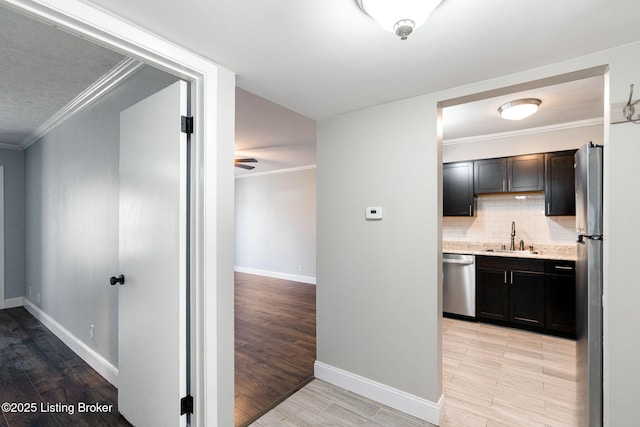 hallway with a sink, baseboards, crown molding, and light wood finished floors