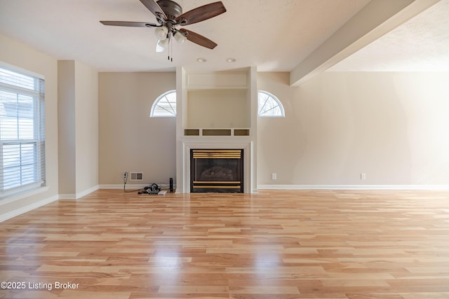 unfurnished living room with visible vents, a ceiling fan, a glass covered fireplace, light wood finished floors, and baseboards