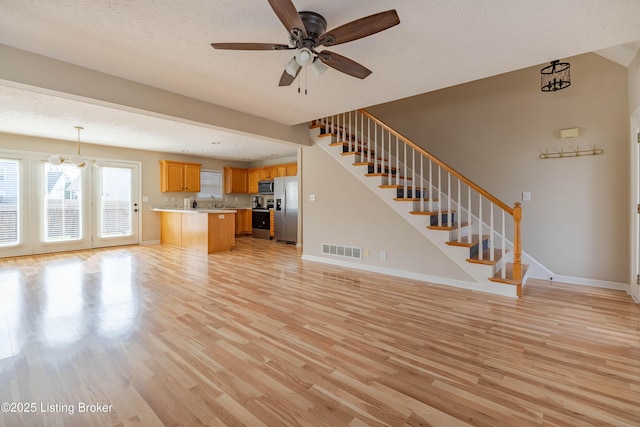 unfurnished living room featuring visible vents, a ceiling fan, light wood-style flooring, and stairs