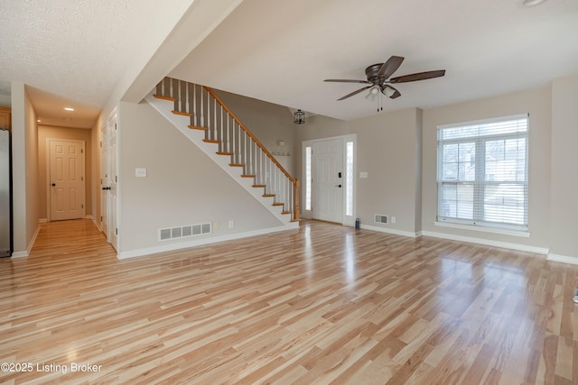 unfurnished living room with visible vents, baseboards, light wood-style floors, and stairs