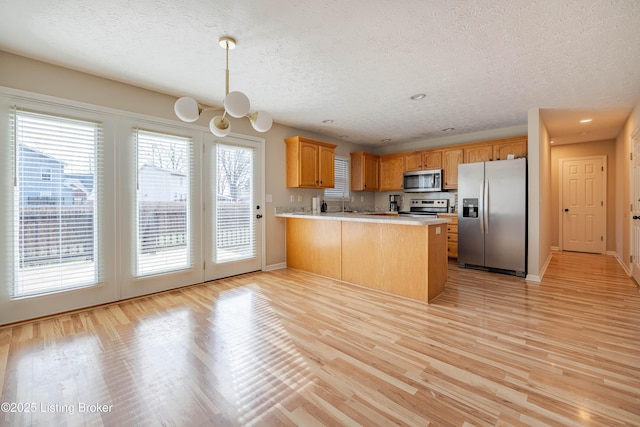 kitchen with a notable chandelier, light wood-style flooring, stainless steel appliances, a peninsula, and light countertops