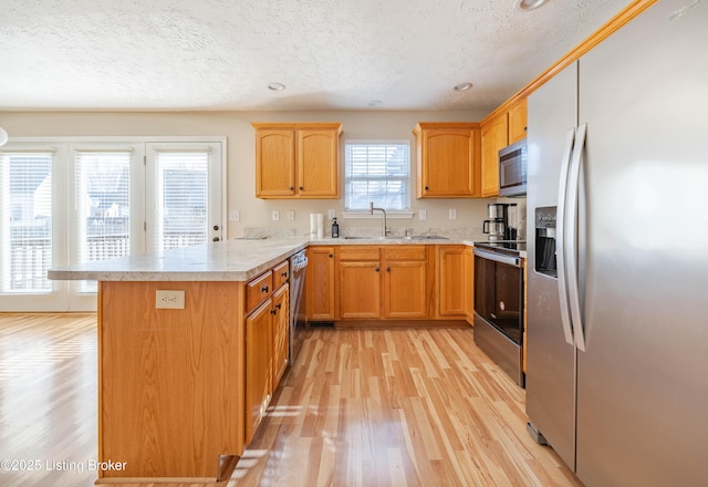 kitchen with light wood-style flooring, a sink, stainless steel appliances, a peninsula, and light countertops