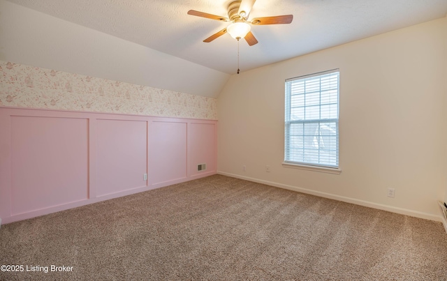 interior space with visible vents, a ceiling fan, carpet flooring, wallpapered walls, and vaulted ceiling