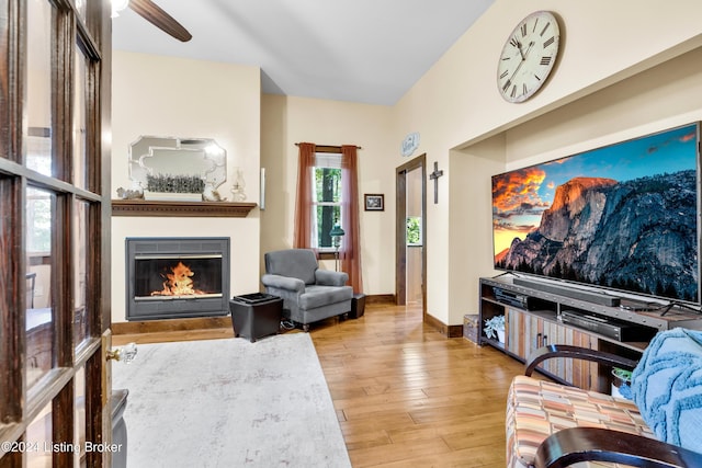 living room featuring a glass covered fireplace, baseboards, ceiling fan, and wood finished floors
