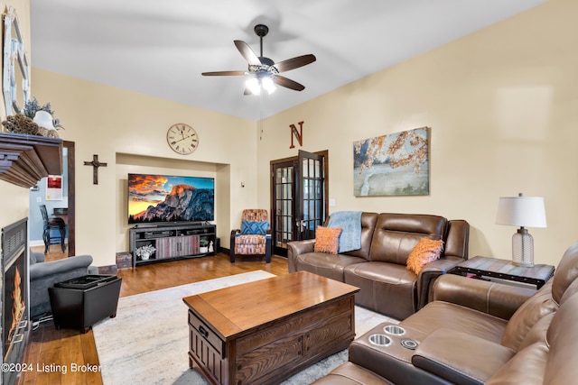 living room with baseboards, a warm lit fireplace, wood finished floors, and a ceiling fan