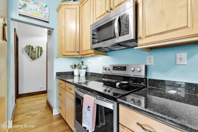 kitchen featuring light brown cabinetry, light wood-style flooring, stainless steel appliances, and dark stone countertops