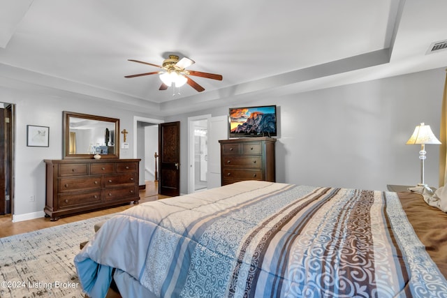 bedroom with a ceiling fan, wood finished floors, visible vents, baseboards, and a raised ceiling