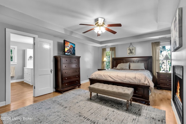 bedroom featuring multiple windows, a ceiling fan, baseboards, and light wood finished floors