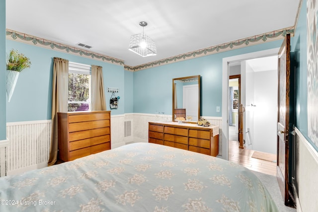 bedroom featuring a wainscoted wall and visible vents