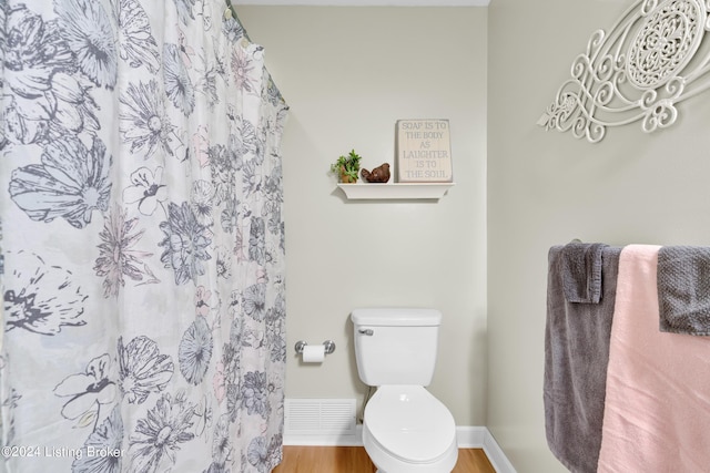 bathroom featuring a shower with shower curtain, wood finished floors, visible vents, baseboards, and toilet