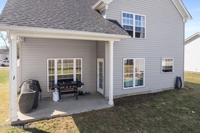 rear view of house with a patio, a yard, and a shingled roof