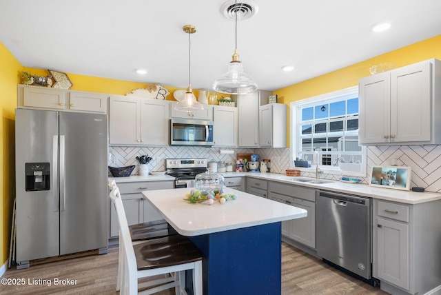 kitchen featuring visible vents, a kitchen island, light countertops, light wood-type flooring, and appliances with stainless steel finishes