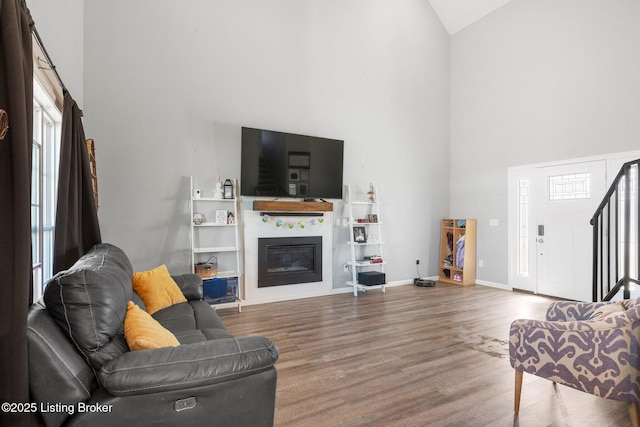 living room with wood finished floors, baseboards, high vaulted ceiling, stairs, and a glass covered fireplace