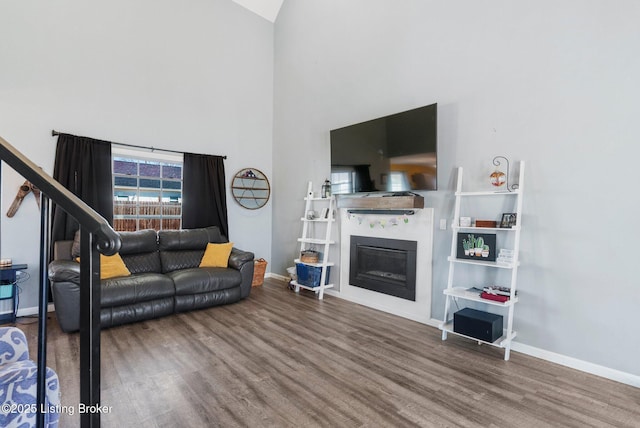 living area featuring a glass covered fireplace, a high ceiling, baseboards, and wood finished floors