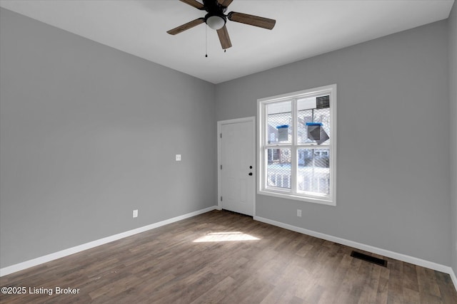 spare room featuring visible vents, ceiling fan, baseboards, and dark wood-style flooring