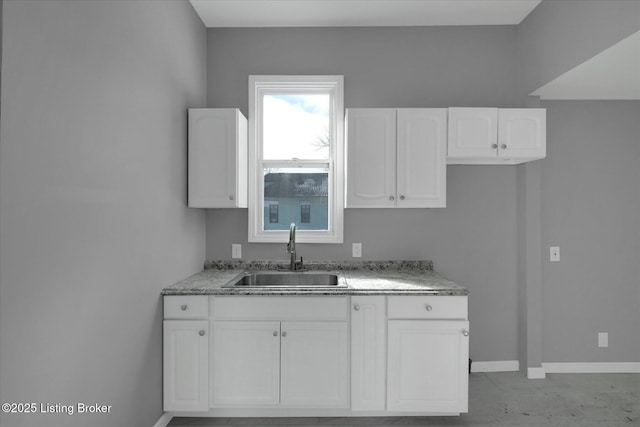 kitchen featuring white cabinetry, light stone counters, baseboards, and a sink