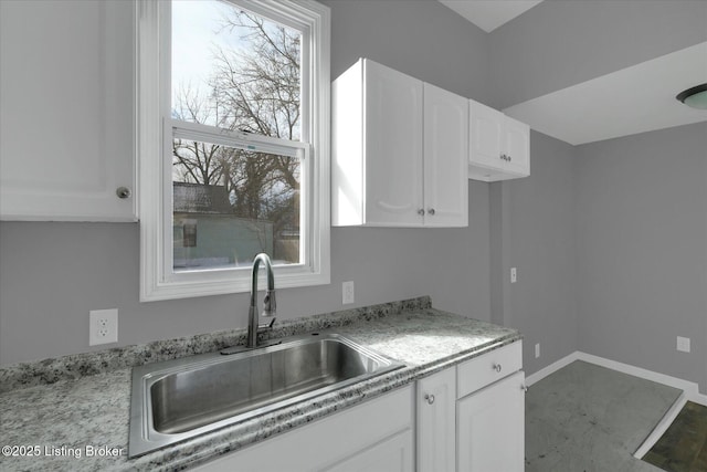 kitchen with white cabinets, baseboards, and a sink