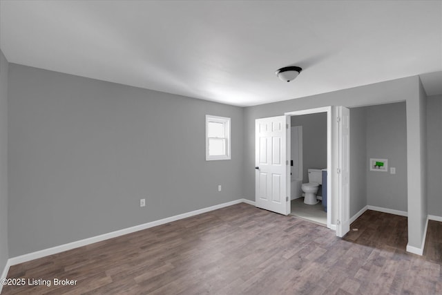 unfurnished bedroom featuring ensuite bath, wood finished floors, and baseboards