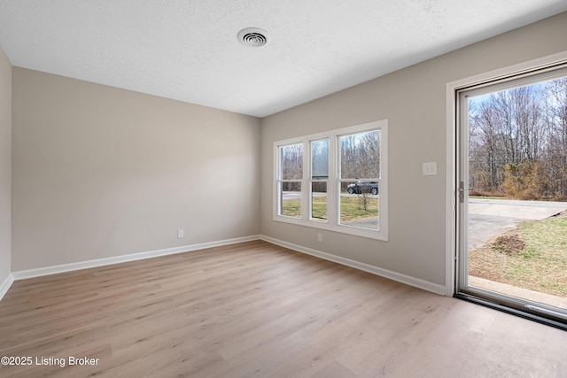 spare room with a textured ceiling, baseboards, and light wood-style floors